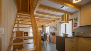 Eine moderne Küche mit Holzbalken, einer zentralen Kochinsel und einer Treppe, die in ein Obergeschoss führt.