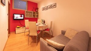 Un espace de vie compact comprenant un coin repas, un canapé, un téléviseur et un mur d’accent rouge.