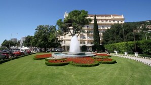 Un hôtel doté d’une fontaine dans la cour, entouré de jardins bien entretenus et surplombé d’un ciel d’un bleu éclatant.