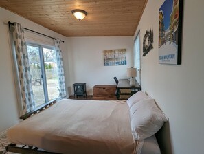 A bedroom with a bed, a desk, a chair, a lamp, a heater, and a window with curtains.