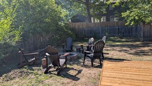 Ein Garten mit Holzterrasse, Feuerstelle und Gartenmöbeln.