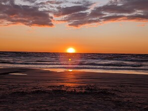 Un coucher de soleil sur l’océan, les vagues reflétant la lumière du soleil sur la plage.