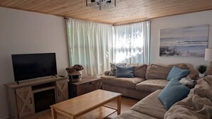 Ein Wohnzimmer mit Fernseher, Sofa, Couchtisch und Vorhängen.