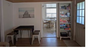 Ein Zimmer mit Holzboden, einem Esstisch mit Stühlen, einem Bücherregal und einer Tür zu einem anderen Raum.
