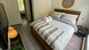 Une chambre à coucher bien rangée, avec un grand lit, une table de chevet avec une lampe et une porte donnant sur une autre pièce.