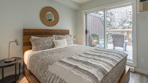 Une chambre avec un grand lit, un miroir rond, une table de chevet et une vue sur une terrasse enneigée, visible à travers une porte-fenêtre coulissante.