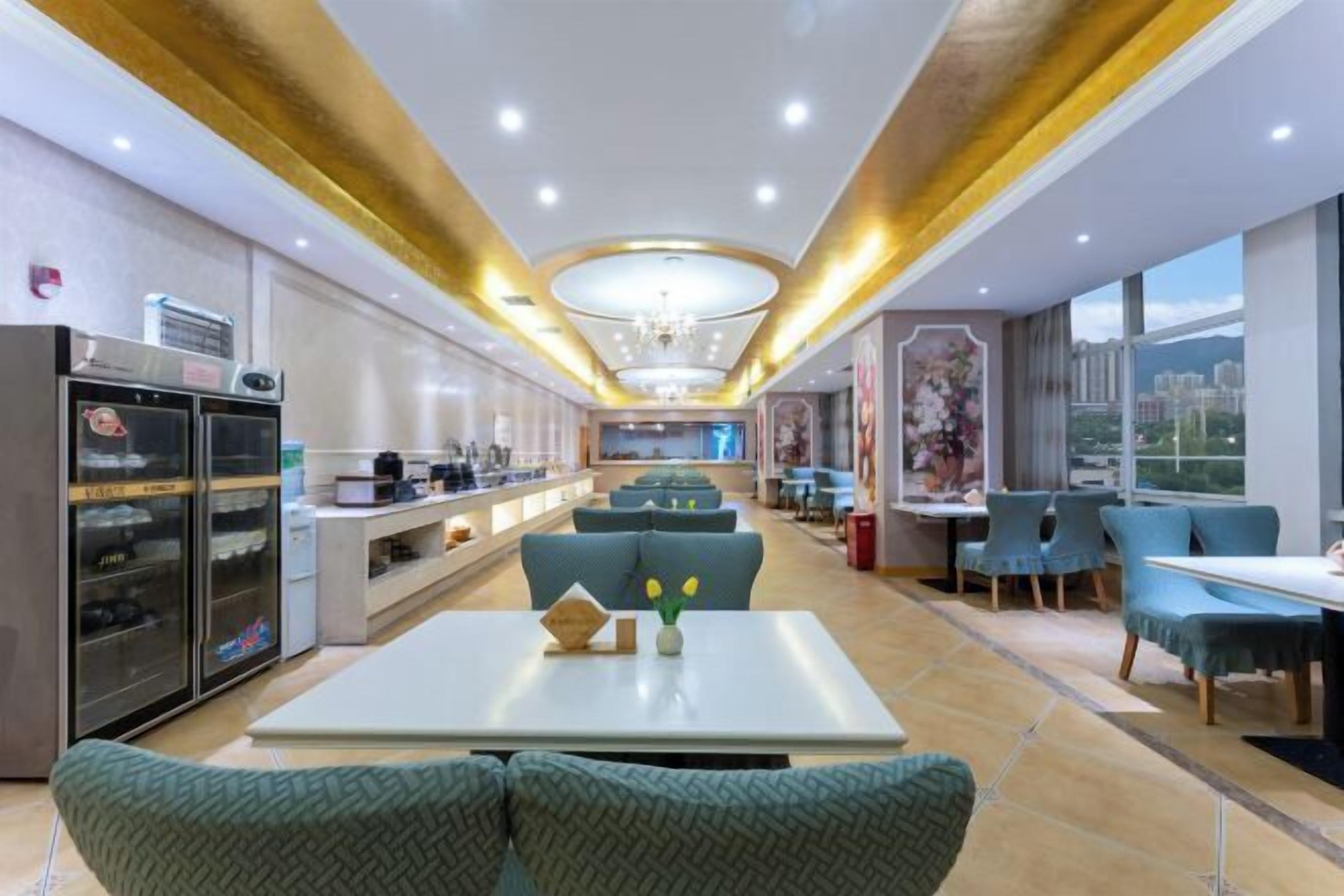 Un moderno vestíbulo de hotel con un área de estar central, una cocina al fondo y grandes ventanales con vistas a la ciudad.