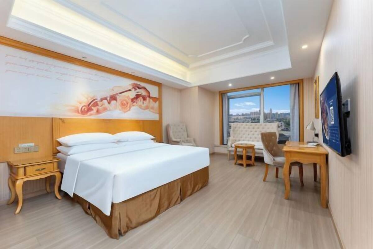 A hotel room with a large bed, a desk, a chair, and a TV.