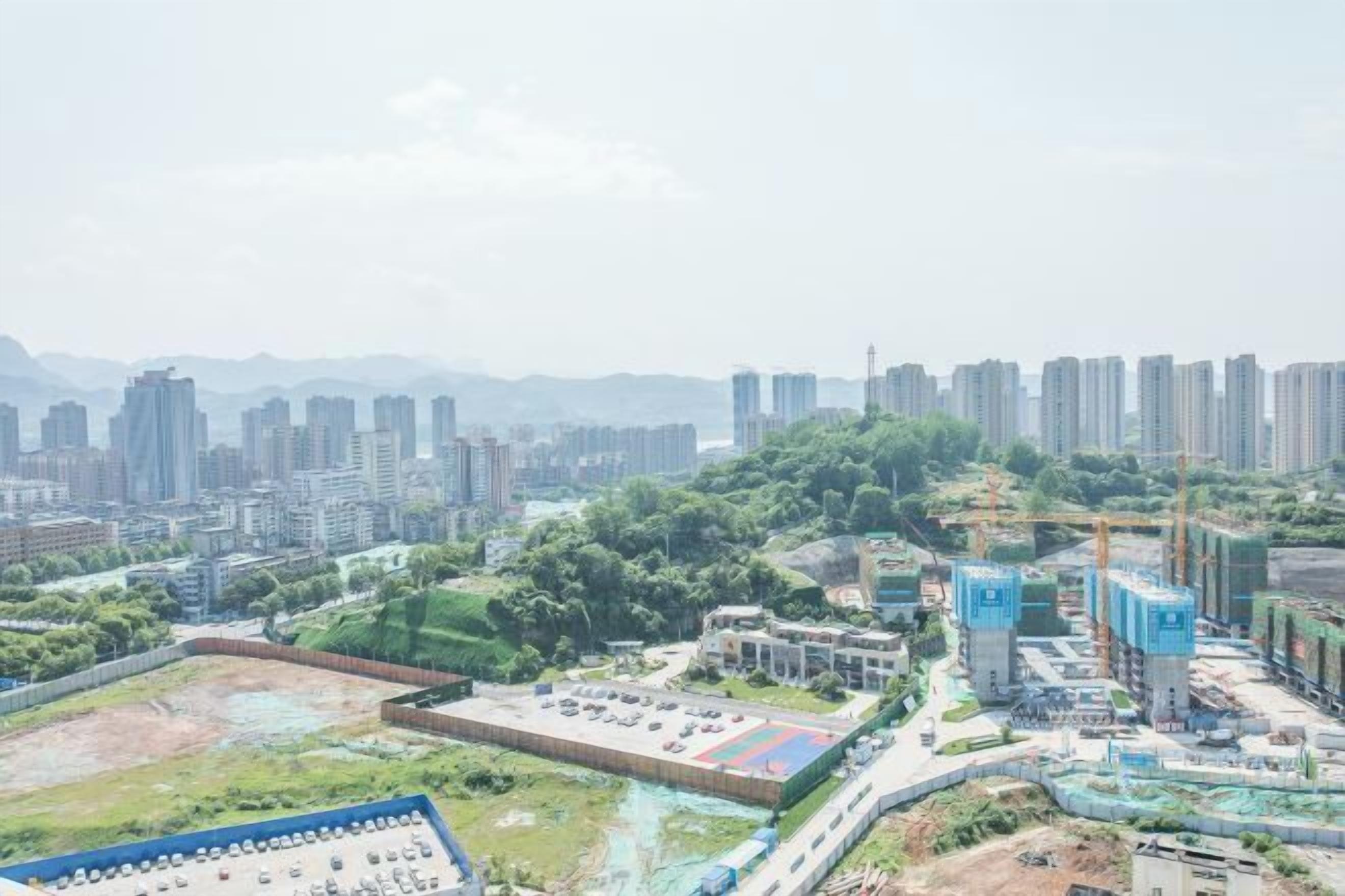 A high-rise building with multiple floors, surrounded by greenery and other buildings.