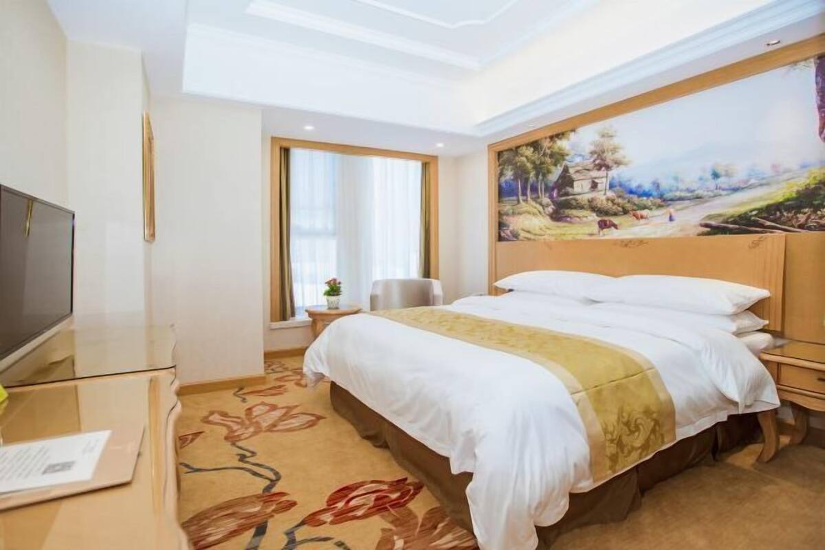 A hotel room with a large bed, a flat-screen TV, a desk, and a painting on the wall.