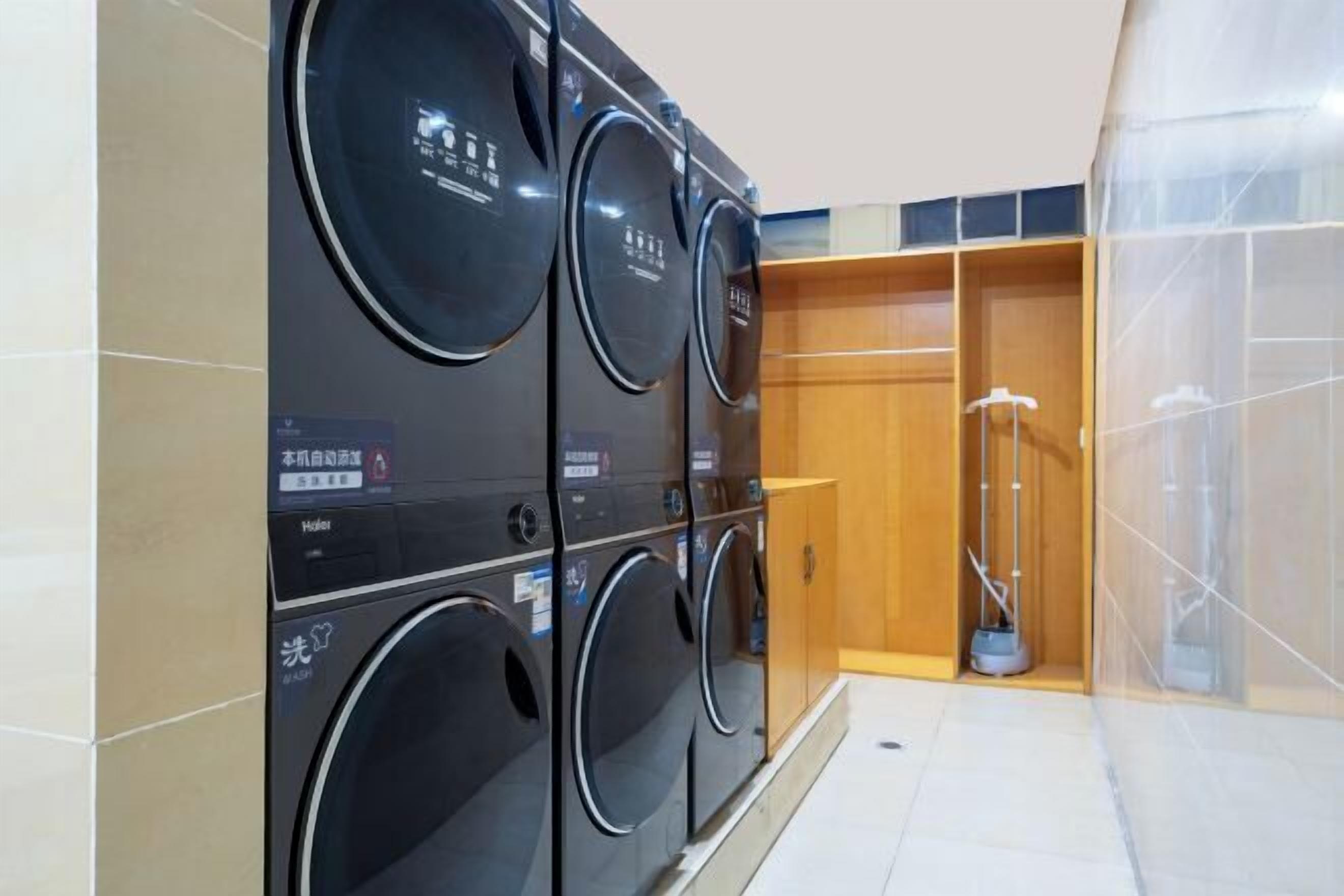A laundry area with multiple washing machines, a mop, and a wooden cabinet.