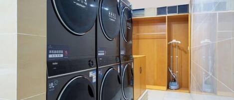 A laundry area with multiple washing machines, a mop, and a wooden cabinet.