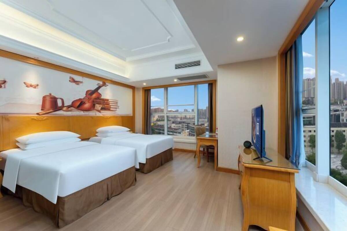 A hotel room with two beds, a desk, a chair, and a TV.