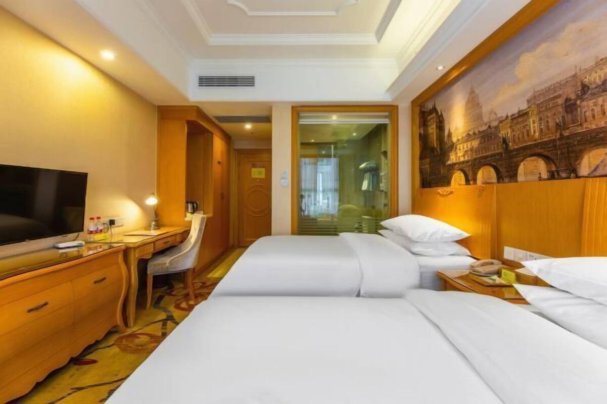 A hotel room with a bed, a desk, a television, and a painting of a bridge.