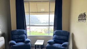 A room with two blue armchairs, a small white table, and a window with curtains.