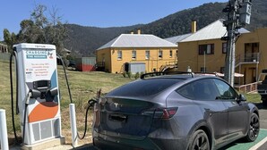 A Tesla Model S charging at a station labeled "CHARGING THE REGIONS" with a sign indicating 100% renewable energy from East Gippsland Shire Council.