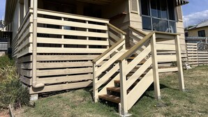 A wooden staircase leading to a covered porch with a window overlooking a grassy area.