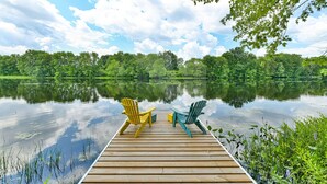 Un muelle de madera que se adentra en un lago tranquilo, con dos sillas Adirondack orientadas hacia el agua.