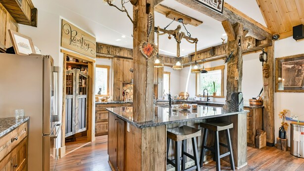 Una cocina rústica con vigas de madera, una isla central con taburetes y un cartel que dice 'Pantry'.