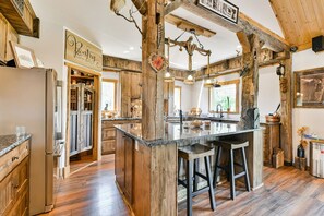 A rustic kitchen with wooden beams, a central island with stools, and a sign reading "Pantry."