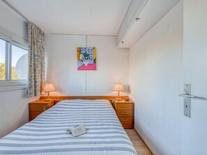 Une chambre à coucher comprenant un lit, deux tables de chevet, une commode, une fenêtre avec des rideaux et un tableau accroché au mur.
