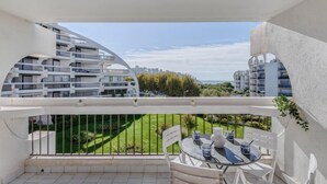 Ein Balkon mit Tisch und Stühlen, Blick auf ein modernes Gebäude und einer grünen Rasenfläche.