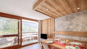 A dining area with a wooden table and chairs, a TV, and a scenic mountain view through large windows. - Palafour (Le Lac) by Interhome (Tignes)