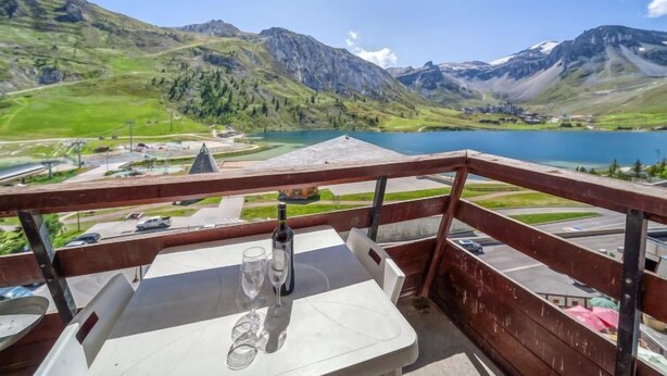 A balcony with a table, two wine glasses, and a bottle, overlooking a lake and mountains. - Palafour (Le Lac) by Interhome (Tignes)