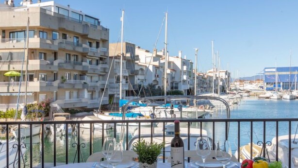 Una mesa preparada para comer, con vista a un puerto deportivo y edificios al fondo.