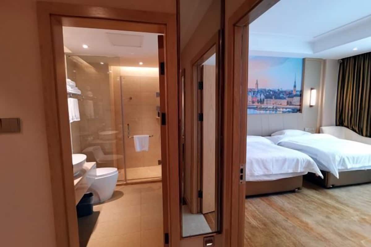 A hotel room with a glass shower enclosure, a bed, and a view of a cityscape.