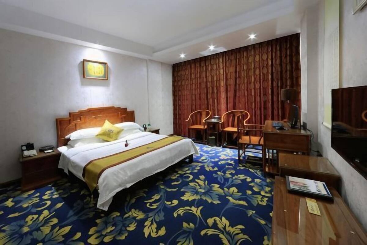 A hotel room with a bed, a desk, a chair, a TV, and a curtain.