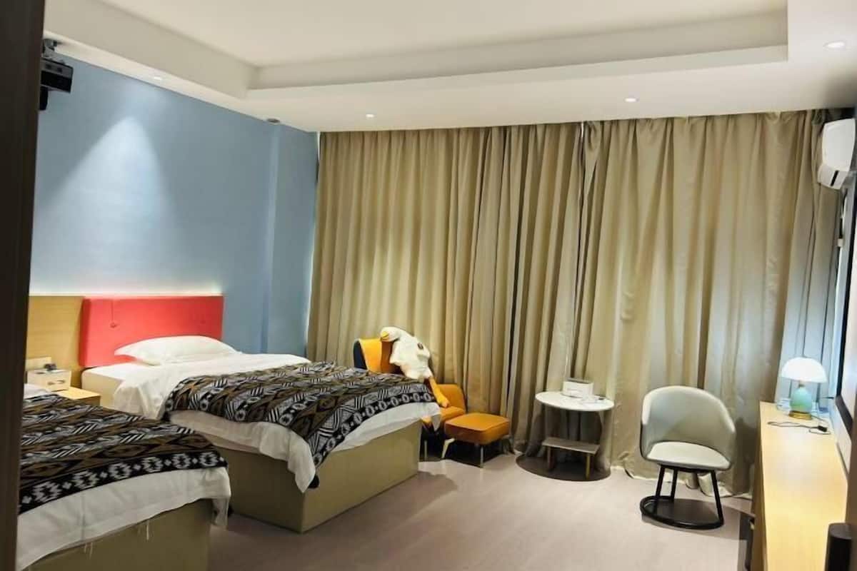 A hotel room with two beds, a desk, a chair, a small table, and a curtain.