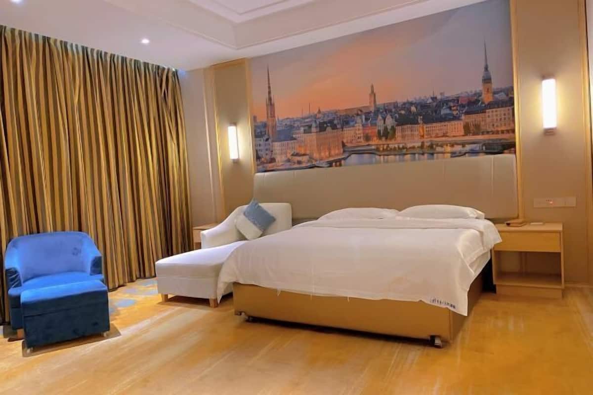 A hotel room with a large bed, a blue armchair, a white sofa, and a cityscape mural on the wall.