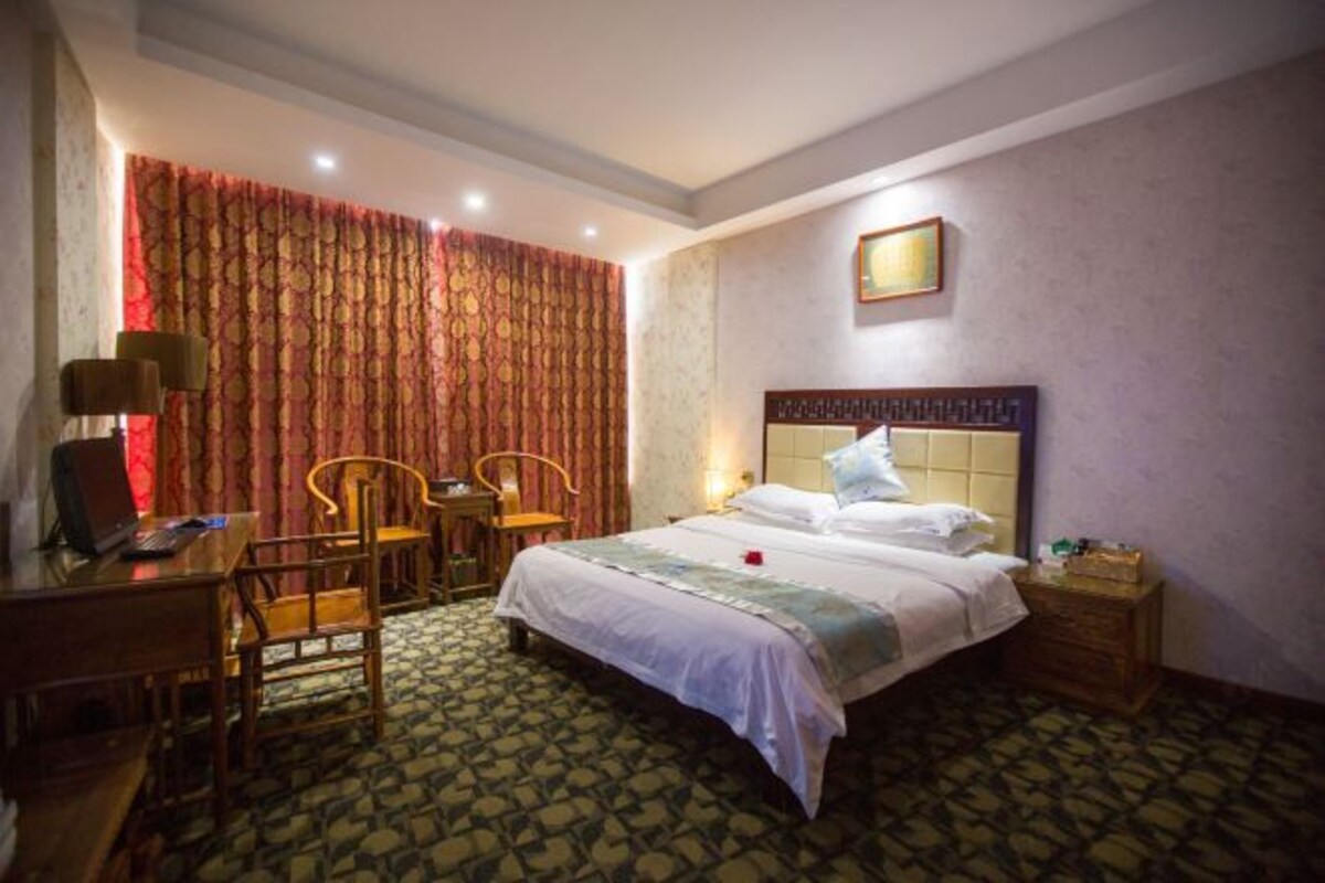 A hotel room with a bed, desk, chairs, and a nightstand.