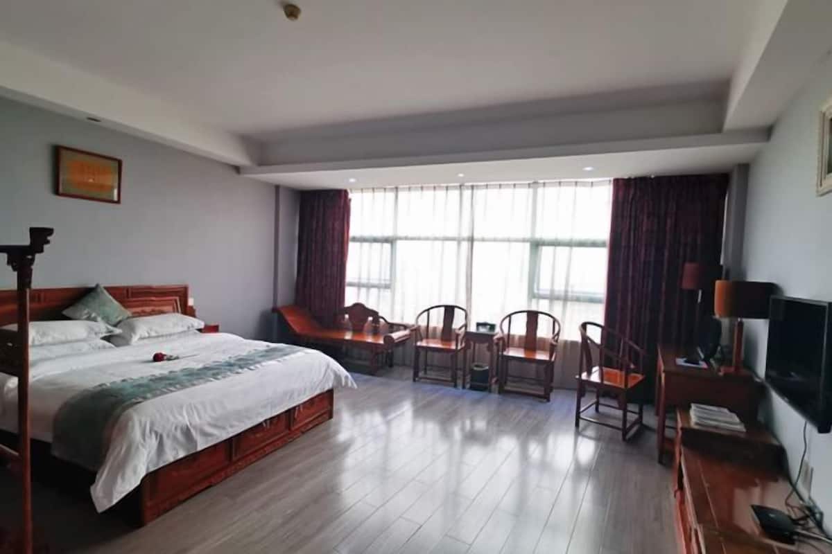 A hotel room with a large bed, a desk with a chair, a television, and a window with curtains.
