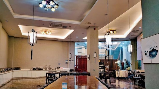 Un hall d’hôtel spacieux, doté d’un long comptoir d’accueil, de plusieurs espaces salon et d’un éclairage moderne suspendu.