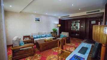 A hotel room with a sofa set, a wooden coffee table, a desk with a computer, and a patterned carpet.