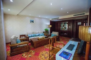 Habitación de hotel con sofá, una mesita de madera, escritorio con ordenador y alfombra estampada.