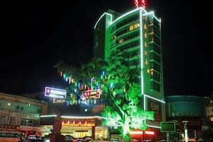 Edifício com vários andares, letreiros iluminados e uma árvore na frente.
