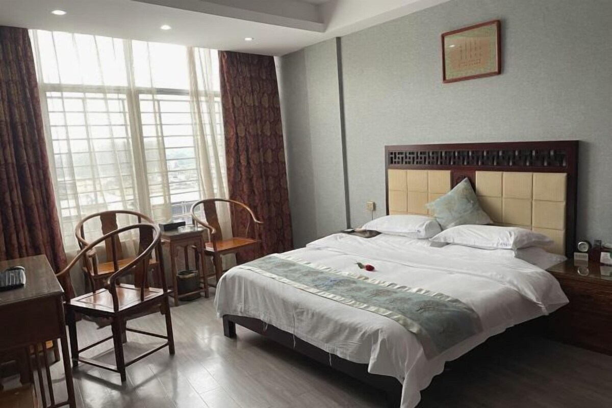 A hotel room with a large bed, a desk with a chair, and a window with curtains.