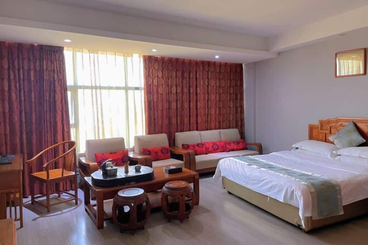 A hotel room with a bed, two sofas, a coffee table, a chair, and a small table with a decorative item.