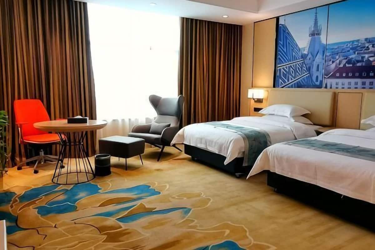 A hotel room with two beds, a red chair, a round table, and a cityscape painting on the wall.