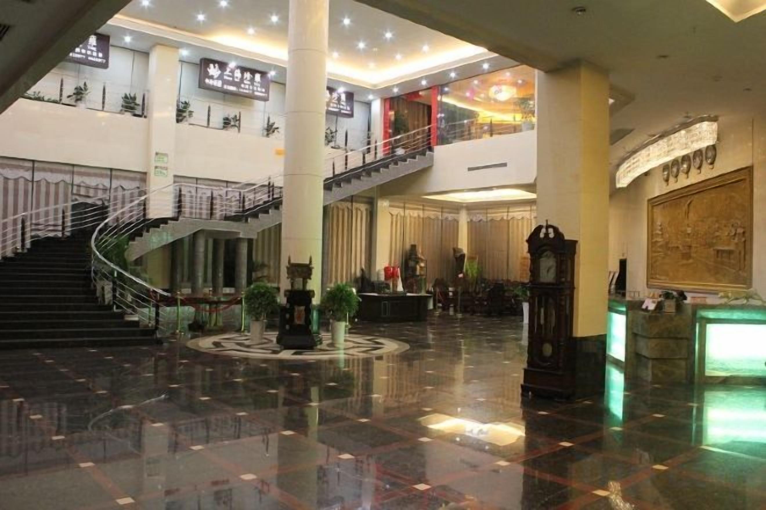 A spacious lobby with a central staircase, a reception desk, and a clock.