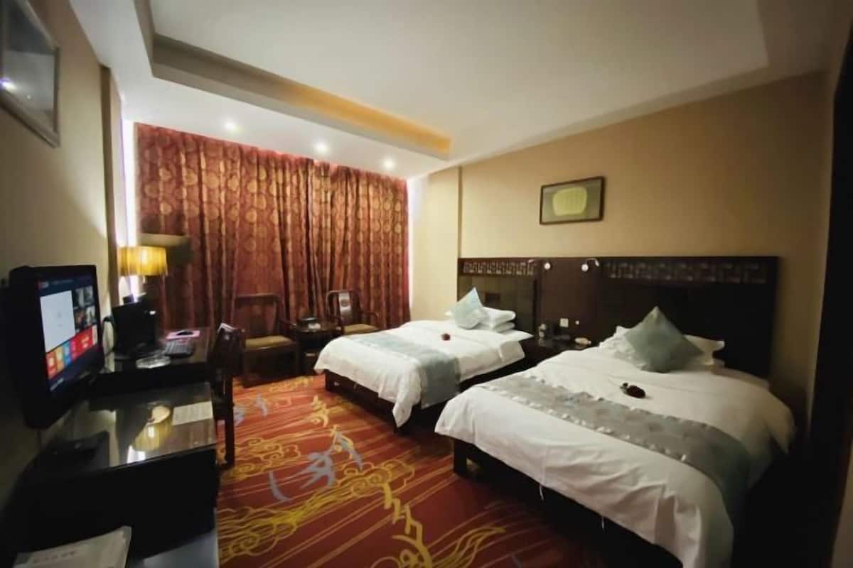 A hotel room with two beds, a desk with a computer, a chair, and a large window with curtains.