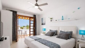 A hotel room with a bed, a desk, a chair, a ceiling fan, and a view of the outdoors. - 2007 Garden Chic, Heated Pool (San Eugenio Alto)