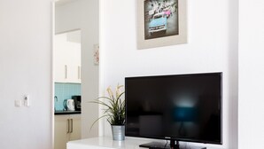 A modern living room with a flat-screen TV on a white cabinet, a potted plant, and a framed picture on the wall. - 2007 Garden Chic, Heated Pool (San Eugenio Alto)