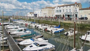 A marina with various boats docked, a waterfront promenade with buildings, and a clear sky. - Résidence Odalys Collection Rève d'Ile by Interhome (Ile de Re)