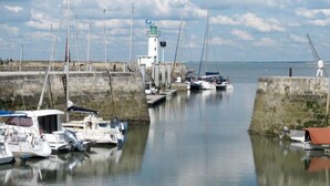 A harbor with boats docked, a lighthouse, and a calm sea under a partly cloudy sky. - Résidence Odalys Collection Rève d'Ile by Interhome (Ile de Re)