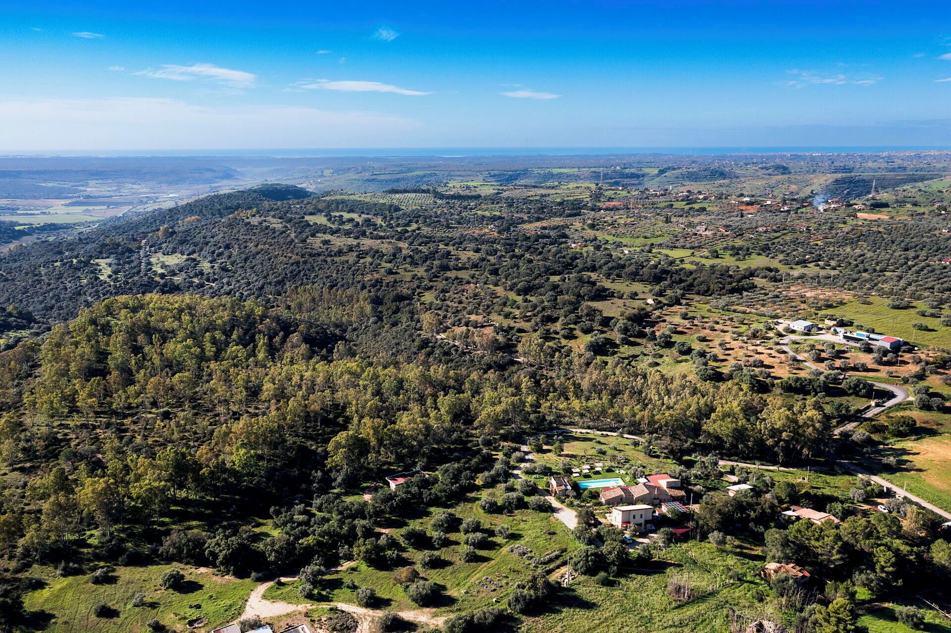 A rural landscape with scattered houses, dense forests, and a winding road.
