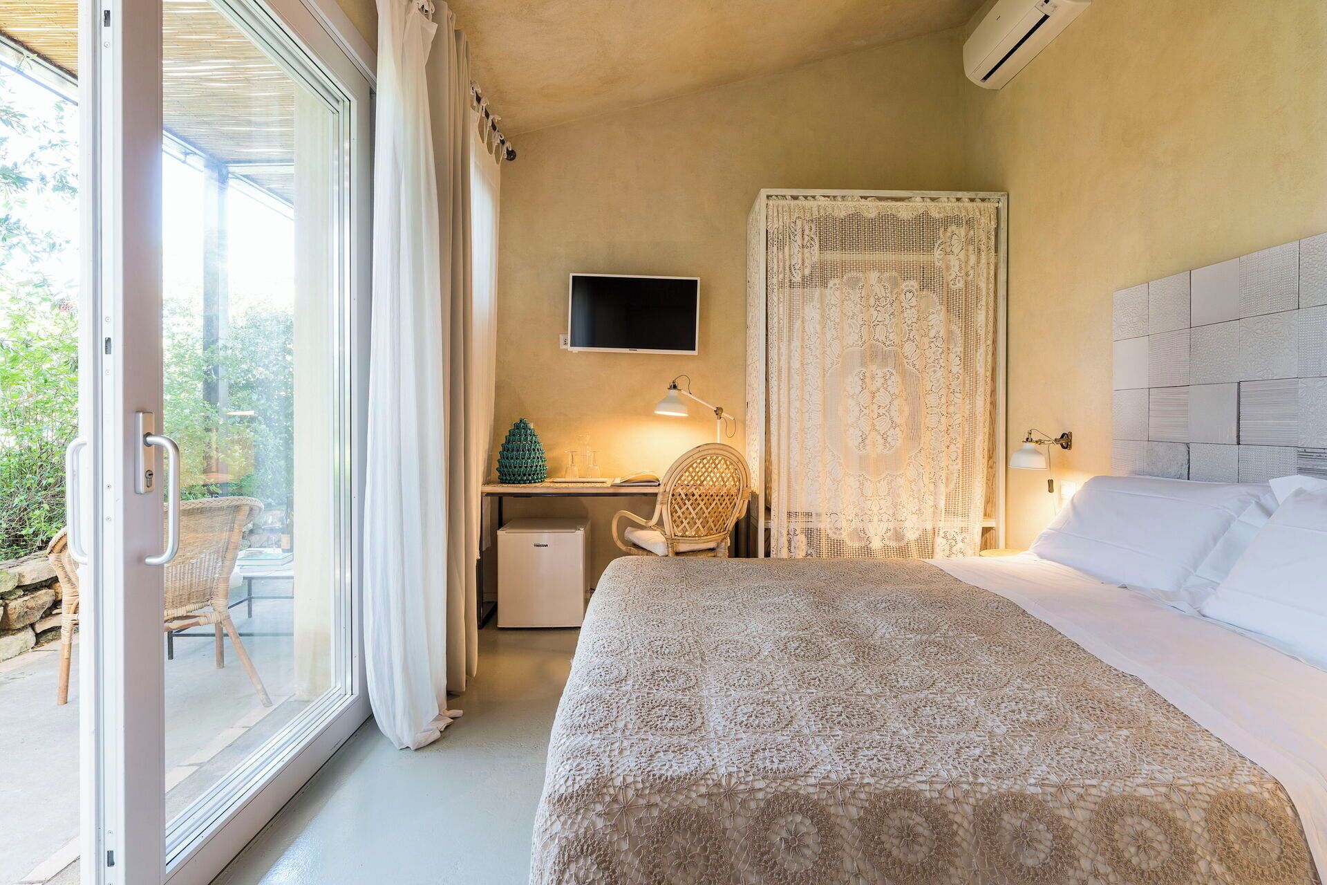 A bedroom with a bed, a desk, a chair, a TV, and a window with curtains.